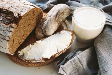 slice of rustic homemade rye flour bread buttered and glass of milk. country food, snack, freshly baked rye bread with butter and milk