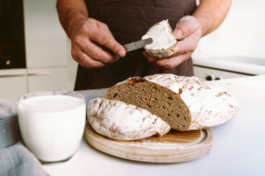 Male hands of cook spreading butter on rye bread in kitchen. Male strong muscular hands of baker, in flour, cut loaf of craft homemade bread from rye flour