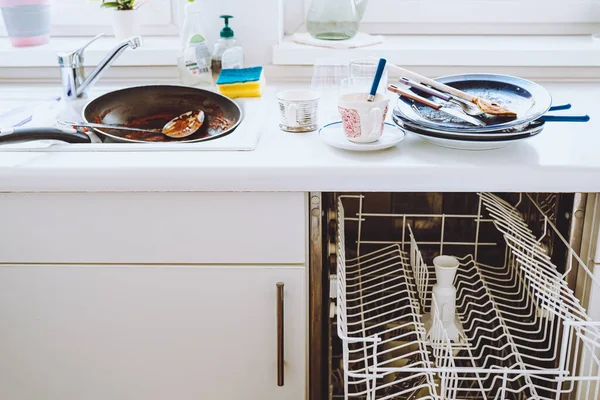 stock image pile of dirty unwashed dishes on kitchen surface, small dishwasher, white kitchen facades. Dirty dishes in kitchen. Small Kitchen with integrated dishwasher, white fronts