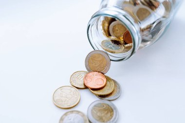 Kavanozdan saçılan Euro sikkeleri. Bozuk paralar beyaz arka planda cam kavanozdan dökülüyor. Kaydetme kavramı.