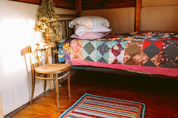 Eski bir köy evinin özgün bir iç mekanı, yatak odası, yastıklı yatak, yamalı battaniye, ahşap parke döşeme, küçük ahşap evde gerçek hayat. Yastıklı yatak ve eski ahşap bir evde yama işi battaniyesi