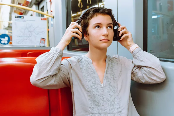 Müzik dinleyerek trenle seyahat et. Kısa kesilmiş saçlı, yüzünde tebessüm olan, kablosuz kulaklık takan genç bir kız trene ya da metroya biniyor, müzikten hoşlanıyor. Metroda kulaklıkla müzik dinleyen genç bir kadın. Seyahat kavramı.