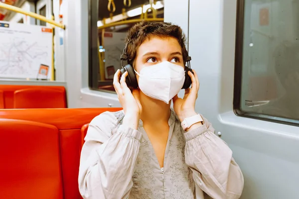 Travel by train listening to music. teenage girl    with short cropped hair, smile on face, wearing wireless headphones, is riding train or subway car, enjoying music. Travel concept