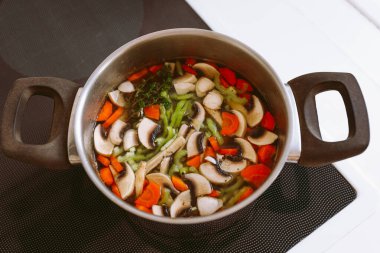 Mantarlı sebze çorbası, havuç ve soğan. Et suyunda vejetaryen sebze çorbası cam elektrikli ocakta tencerede pişirilir.