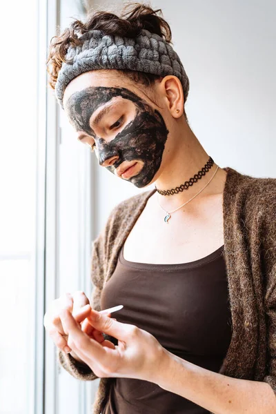 Mladá Žena Kosmetické Černé Masce Obvazem Vlasech Dělá Manikúru Stojí — Stock fotografie