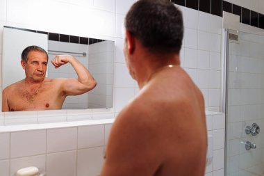 Orta yaşlı bir adam, havluyla, çıplak gövdesiyle, aynada kendine bakar, vücuda hayran olur, pazılarını açar, yüzündeki kırışıklıkları inceler, banyoda, dikiz aynasından bakar.