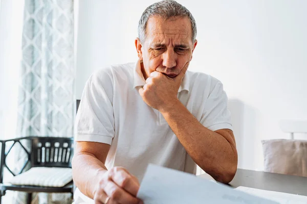 Stock image Middle aged man holding documents reading paper bills, calculating pension fees, payments, taxes, planning family retirement money finances at home. middle-aged man at table at home reading bill