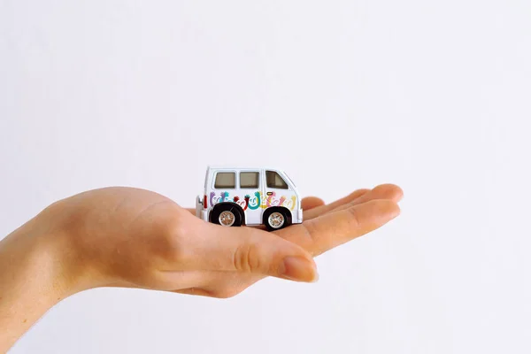 womans hand on white background holds small model of family-type car minibus, concept of insurance, protection, safety