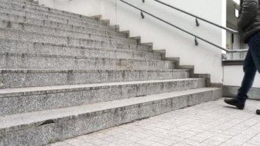 Kotlu ve kışlık çizmeli bir adam taş granit gri merdivenlerde yürür.