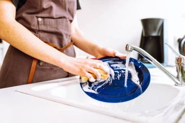 Kahverengi şeflerin önlüklü kadın bulaşık deterjanıyla süngerle yıkıyor, mutfakta lavaboda. konsept temizlik, bulaşık yıkama, bulaşık makinesi