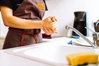 Aşçı önlüğündeki kadın ince figür mutfak lavabosunun yanında duruyor, bulaşık yıkadıktan sonra ev hanımı bulaşıkçısını tutuyor.