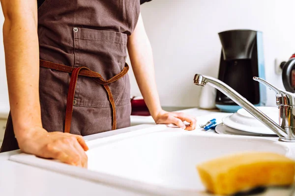 シェフの女性スレンダーな姿は台所の洗面台の近くに立つエプロンや食器洗い機を手に — ストック写真