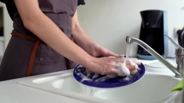 Kahverengi şeflerin önlüklü kadın bulaşık deterjanıyla süngerle yıkıyor, mutfakta lavaboda. konsept temizlik, bulaşık yıkama, bulaşık makinesi
