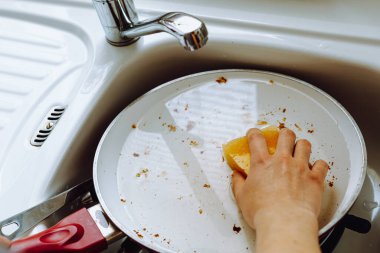 Kadınların elleri, ev mutfağında yağlı, yanmış tavayı seramik kaplama, çamaşır bezi ve bulaşık deterjanıyla yıkıyor. konsept rutin, el işi, bulaşık yıkama.