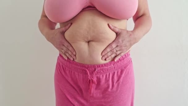 无法辨认的丰满女人在粉色上衣抖动着肥胖的腹部 用手挤压着腹部脂肪 做按摩 瘦身淋巴引流整形手术复制空间 — 图库视频影像