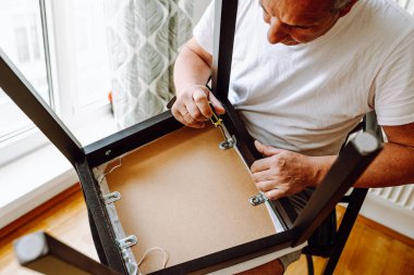 Tornavidayla ahşap sandalyeyi tamir eden adamların eli. Konsept ev sahibi, bir saatliğine tamirci, ev işi. Adam sandalyeyi tornavidayla, vidayla tamir ediyor.