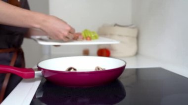 Kadın elleriyle doğranmış sebzeleri tavaya döküyor. Ev mutfağında sebzeli omlet pişirme aşamaları