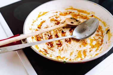 Yakın çekim tavası, yapışmaz seramik kaplamalı, bozulmuş, yanmış yiyeceklerle birlikte, bir elektrikli ocağın üzerinde duruyor. Kirli kızartma tavası, seramik kaplamalı, kalıntıları yanmış yiyeceklerle