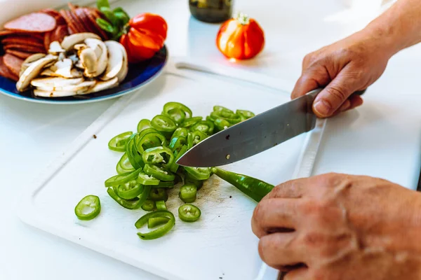 stock image Male hands with large kitchen knife cuts green long chili pepper in home kitchen