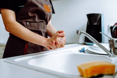 Aşçı önlüğündeki kadın ince figür mutfak lavabosunun yanında duruyor, bulaşık yıkadıktan sonra ev hanımı bulaşıkçısını tutuyor.