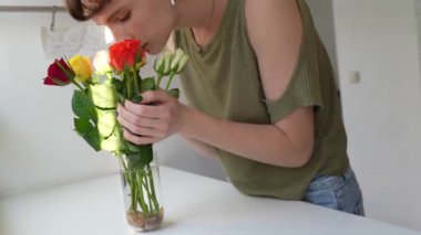 Çekici, narin bir genç kız, gül çiçekleriyle ilgileniyor, buket, vazoda su değiştiriyor, mutfakta duruyor. Rose çiçek bakımı talimatlarını kesti. Budama sapı, düzenleme buketi