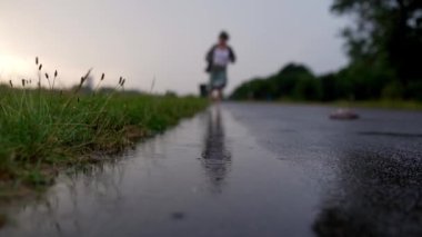 Kadın bacakları, ergen bacakları, su birikintilerinde çıplak ayakla koşmak, yağmurda, gün batımında. Yağmurda çıplak ayakla su birikintilerinde koş. Eğlence, özgürlük, doğa ve bacak sağlığı kavramı
