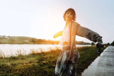 Su birikintilerinde çıplak ayakla dans eden Happy portresi, genç kız, ıslak saçlı, bol yaz kıyafetleri içinde, gün batımında, yağmurdan sonra, nehir kenarında. Doğadan zevk alma kavramı, gün batımı, özgürlük,