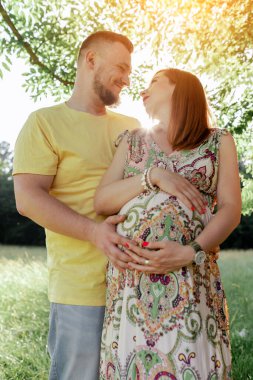 Gün batımında güzel müstakbel ebeveynlerin portresi. Genç, güzel, kızıl saçlı hamile bir kız, sakallı bir koca, güneşin altında duran doğaya karşı duran bir erkek.