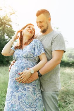 Gün batımında güzel müstakbel ebeveynlerin portresi. Genç, güzel, kızıl saçlı hamile bir kız, sakallı bir koca, güneşin altında duran doğaya karşı duran bir erkek.