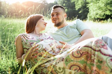 Gün batımında güzel müstakbel ebeveynlerin portresi. Genç, güzel, kızıl saçlı hamile bir kız, sakallı bir koca, güneşin altında duran doğaya karşı duran bir erkek. 