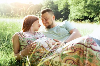Gün batımında güzel müstakbel ebeveynlerin portresi. Genç, güzel, kızıl saçlı hamile bir kız, sakallı bir koca, güneşin altında duran doğaya karşı duran bir erkek. 