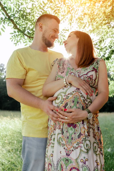 Gün batımında güzel müstakbel ebeveynlerin portresi. Genç, güzel, kızıl saçlı hamile bir kız, sakallı bir koca, güneşin altında duran doğaya karşı duran bir erkek.