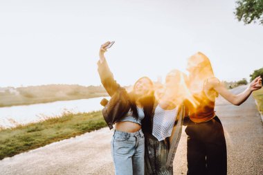 Doğada eğlenen genç kızlar. Genç kadınlar, genç kızlar, sırıtan, yağmurdan sırılsıklam olmuş saçlarıyla, eğlenen, nehirde selfie çeken ve dans eden güneş ışınları, parıldayan lensler...