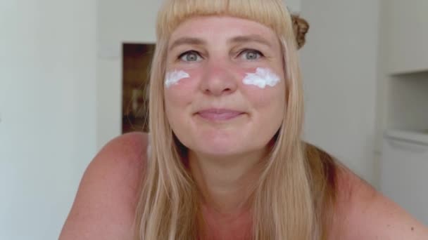 Attraktiv Medelålders Kvinna Med Blont Långt Hår Smetar Fuktighetskräm Ansiktet — Stockvideo