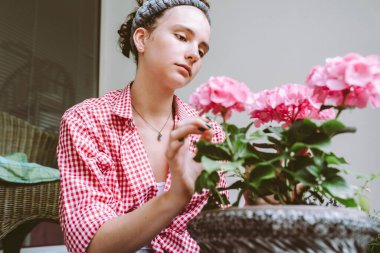 Genç bir kadın saksıdaki ortancayla ilgileniyor, balkonda oturuyor. Hobiler, bahçecilik.