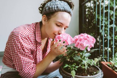Genç bir kadın saksıdaki ortancayla ilgileniyor, balkonda oturuyor. Hobiler, bahçecilik.