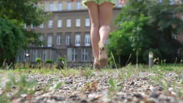 美しい細い足の若い女性が砂利道街に沿ってハイヒールの靴を履いて歩く スローモーション 生態系の自然のパスを歩いてください 裸足でヒールの高い靴を履いた夏 — ストック動画