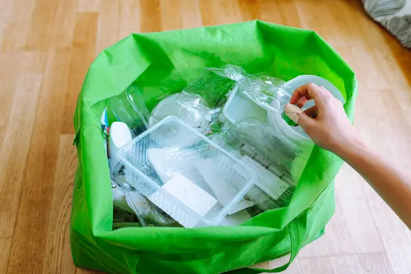 young woman sorts plastic at home, puts plastic bottles in reusable fabric ecological bag. Sorting garbage at home