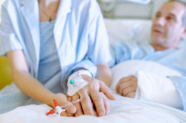 Klinik çalışanları yatalak hastalarla ilgilenir. Orta yaşlı bir adam, kırık kollu, yatağa uzanmış, genç bir kız yanında duruyor, hastaya bakıyor. Hastanedeki hasta bakımı ve bakımı