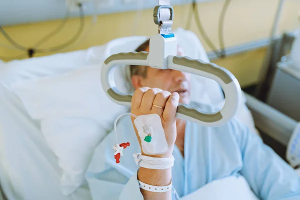 Uyumlu bir hastane yatağında oturan orta yaşlı bir adam yardım çağırmak için korkuluklara tutunuyor. Hastane odası için konfor ekipmanı