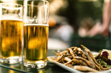 İki bardak bira, camda köpük, kızarmış ançüez ya da sprat, bulanık yeşil mahsulde.