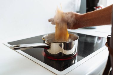 Erkekler spagettiyi sıcak suya bandırır. Ev mutfağındaki seramik hob 'un üzerinde durur.