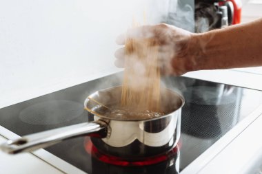 Adam evde, mutfakta makarna pişiriyor. Kahverengi önlüklü bir adam spagettiyi dener, spagettiyi kaynamış suyun üzerinde özel kaşıkta tutar. İtalyan ev yemeği konsepti