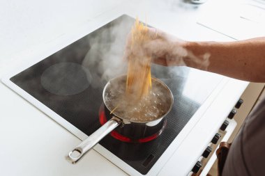Erkekler spagettiyi sıcak suya bandırır. Ev mutfağındaki seramik hob 'un üzerinde durur.