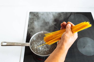 Erkekler spagettiyi sıcak suya bandırır. Ev mutfağındaki seramik hob 'un üzerinde durur.