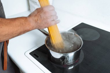 Erkekler spagettiyi sıcak suya bandırır. Ev mutfağındaki seramik hob 'un üzerinde durur.