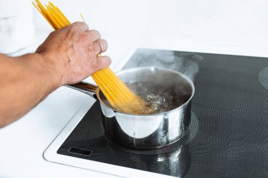 Erkekler spagettiyi sıcak suya bandırır. Ev mutfağındaki seramik hob 'un üzerinde durur.