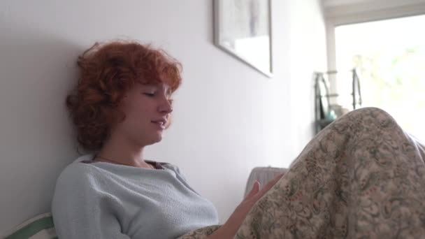 Lockigt Rödhårig Tonåring Flicka Pyjamas Sitter Sängen Använder Mobil Grimaser — Stockvideo