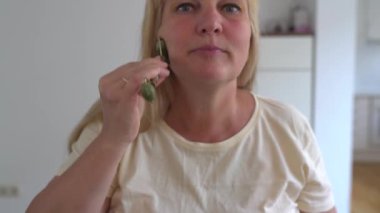 Çekici orta yaşlı kadın, sarışın, cilt yüzeyine bir pipetle kozmetik kolajen uyguluyor, masaj yapıyor, kırışıklıkları düzleştiriyor, masaj yüzü, yaşla ilgili sarkık yanakları yok ediyor.