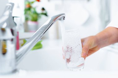 Kadınların elleri mutfaktaki musluğun yanında temiz su bardağını tutuyor. Nehir suyu cama dökülür.